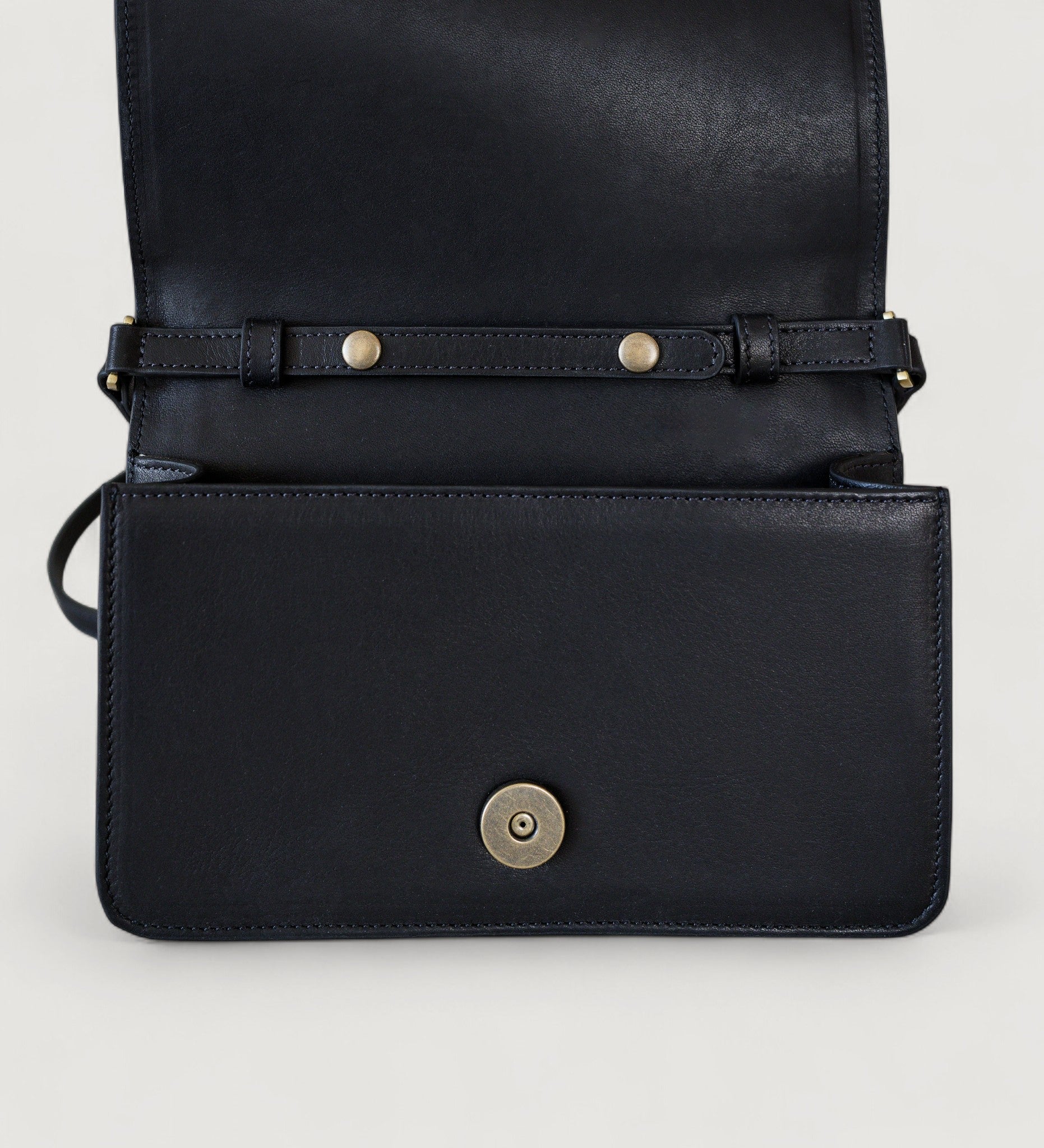 Black leather bag with a strap and metal buckle on a light gray background