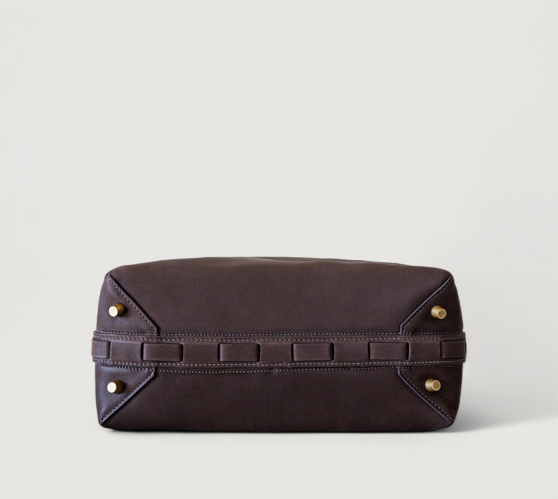 Bottom view of a brown leather clutch bag with brass feet on a light gray background
