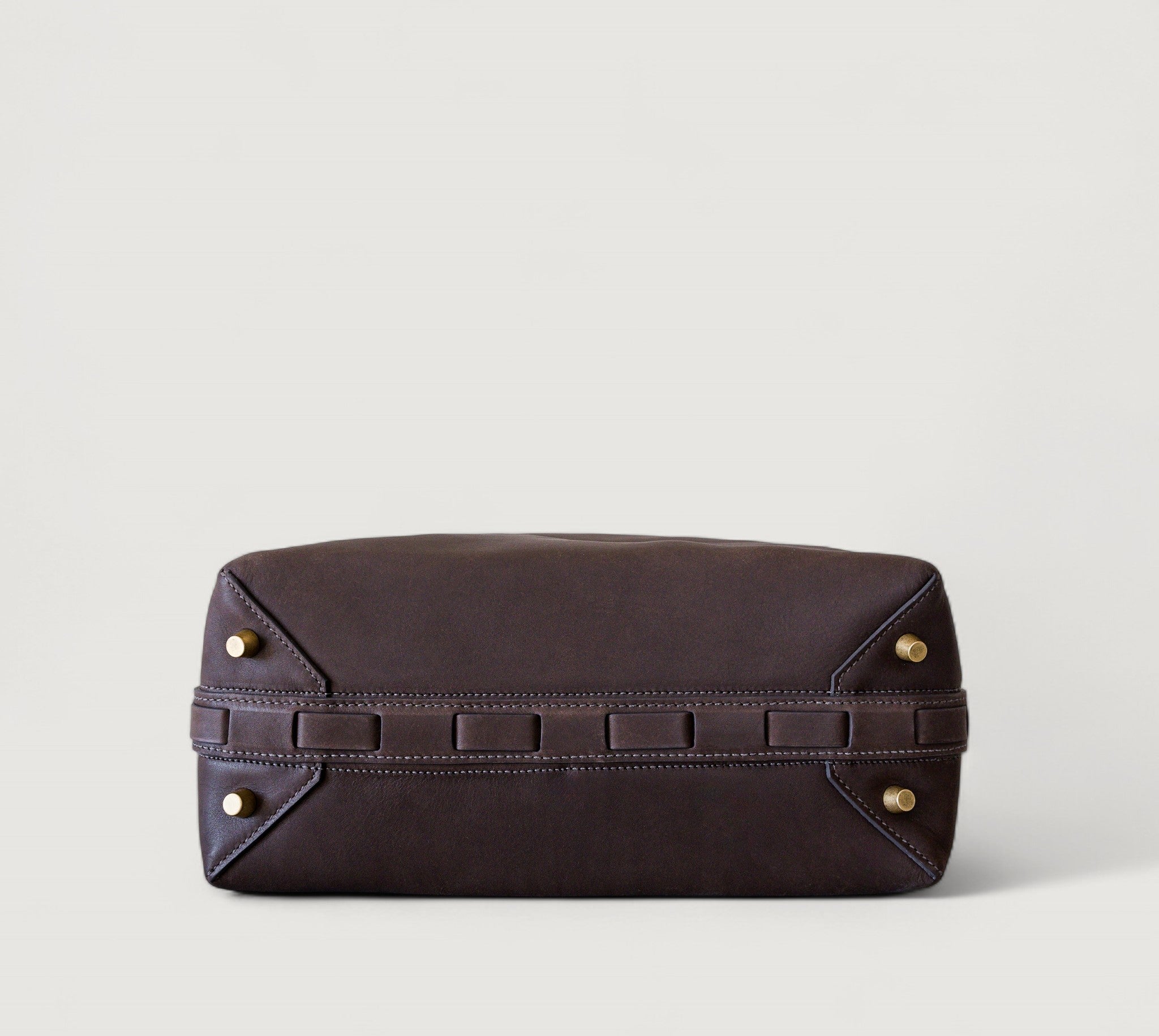 Bottom view of a brown leather clutch bag with brass feet on a light gray background