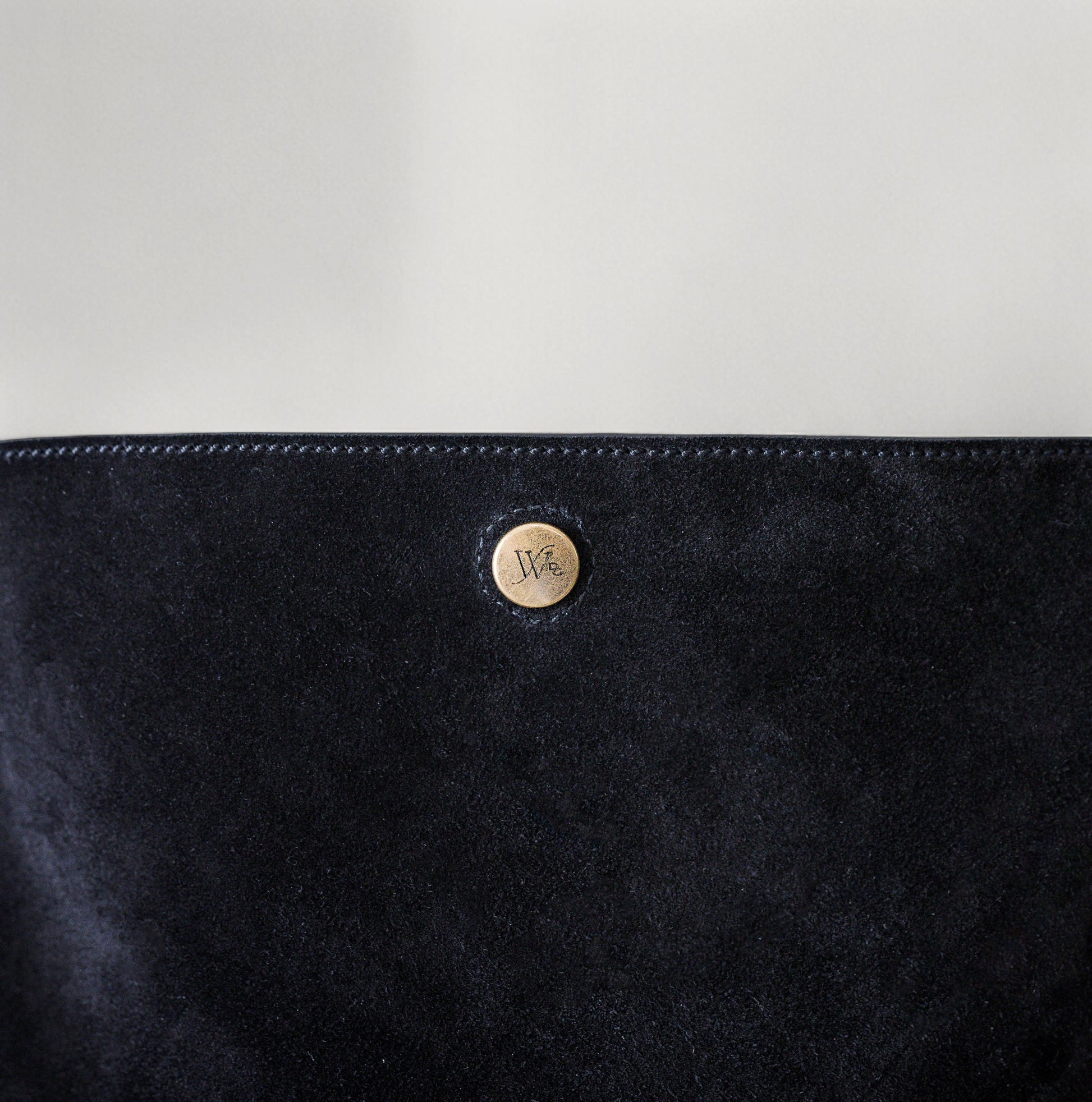 Close-up of black suede with a brass button featuring a logo on a light gray background.