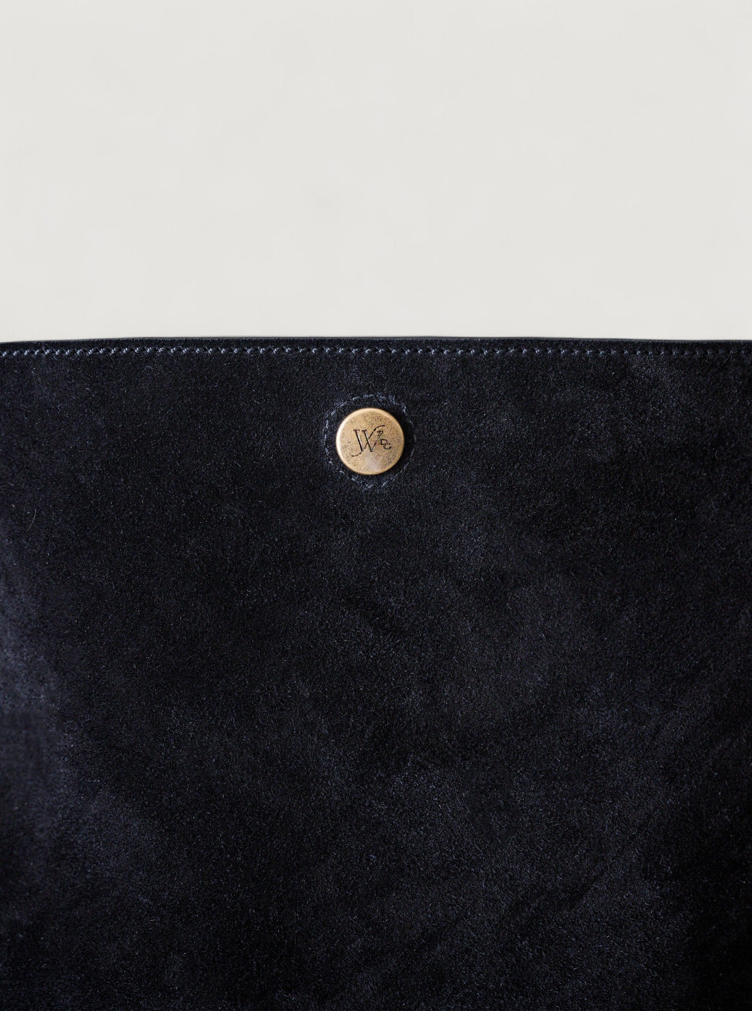 Close-up of a black textured surface with a brass button featuring a logo.