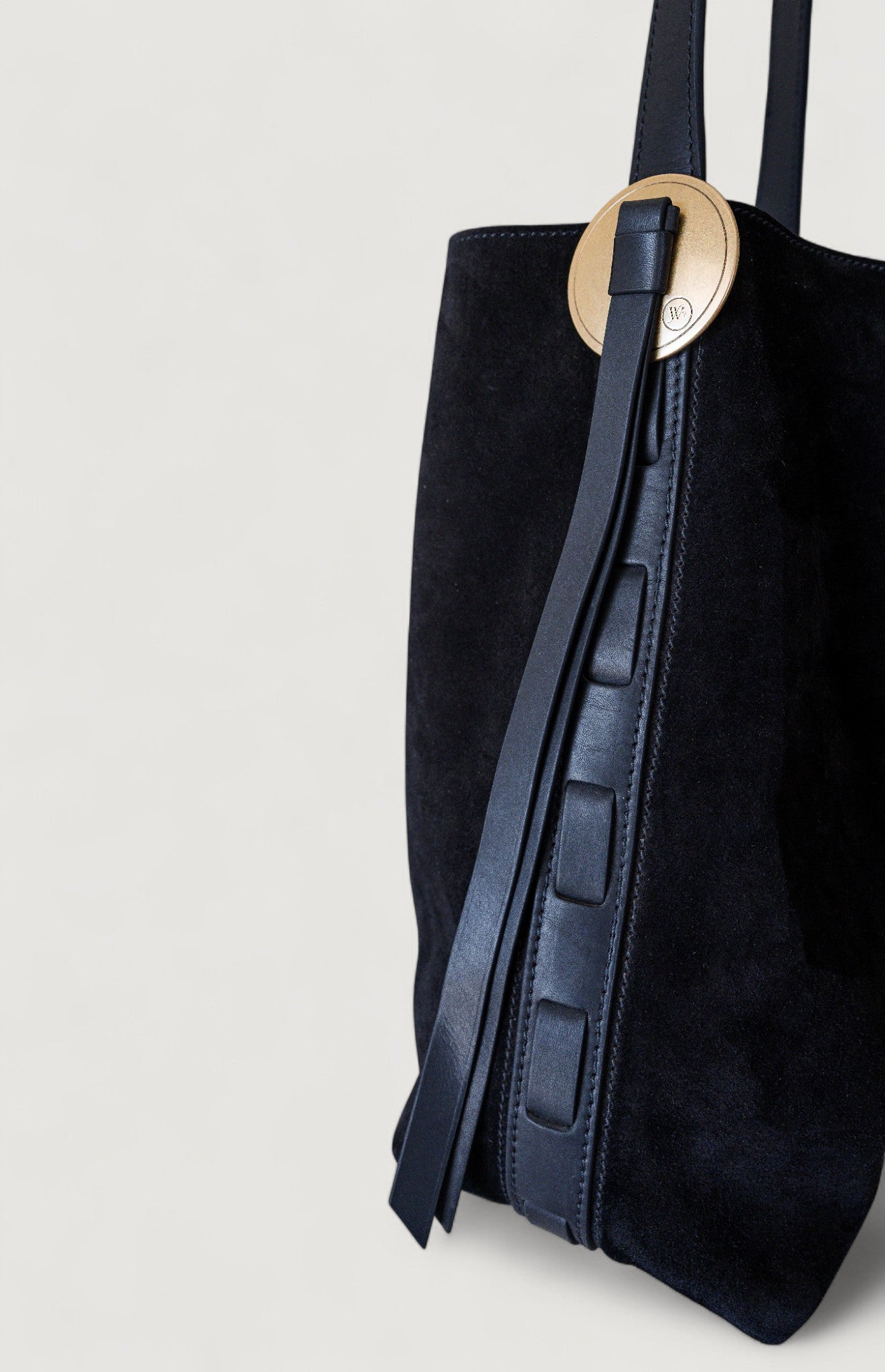 Black tote bag with a brass concho on a light gray background