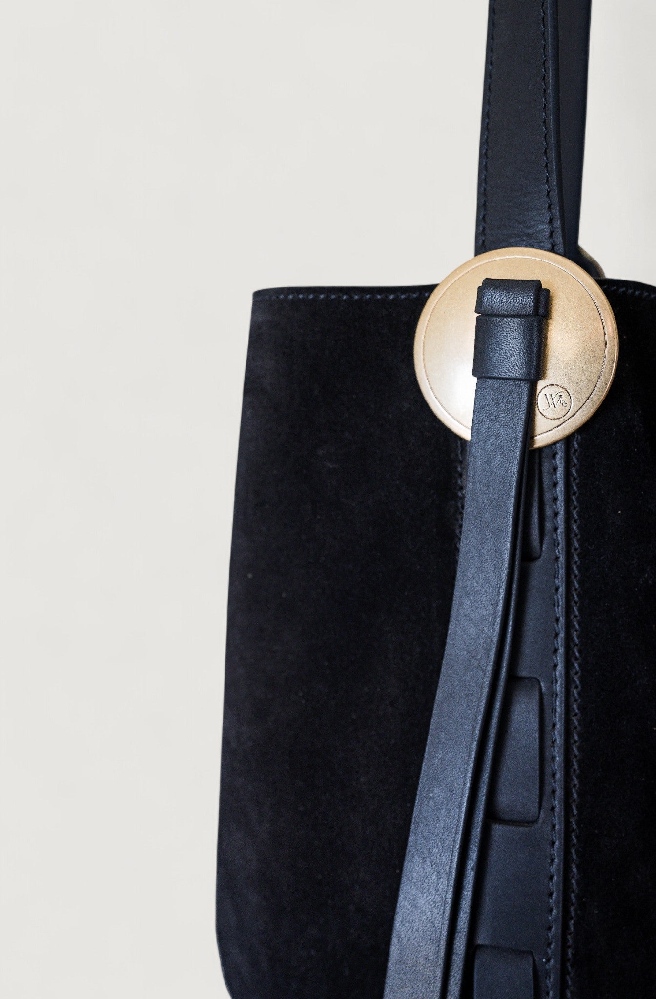 Black suede handbag with a brass concho on a white background