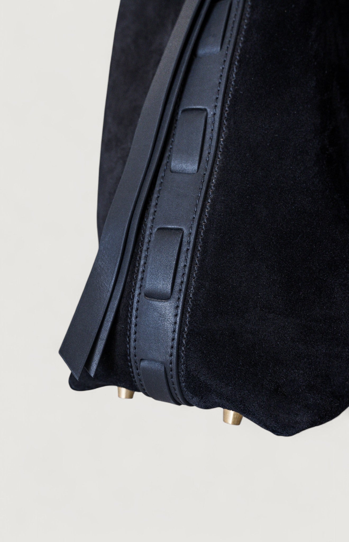 Close-up of a black leather bag with brass feet on a light gray background