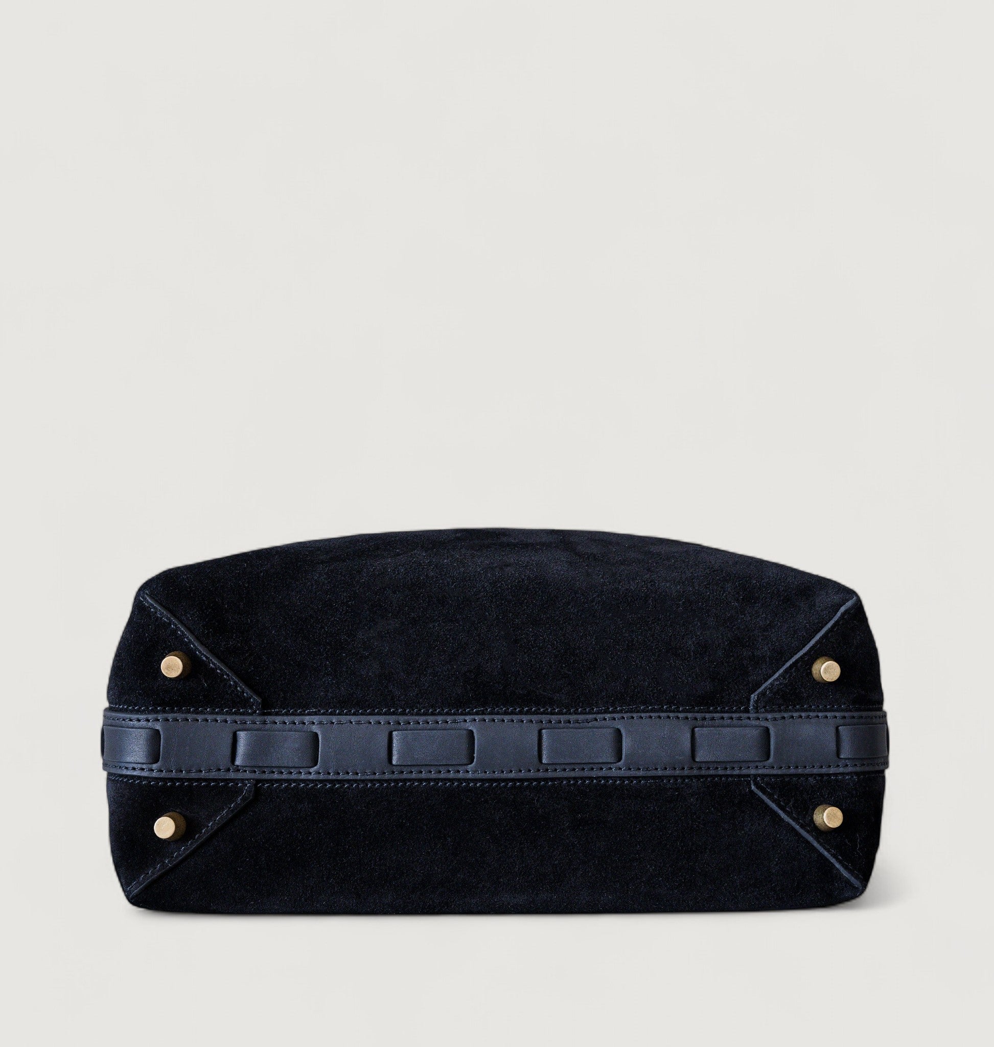 Bottom view of a black leather bag with brass feet on a light gray background