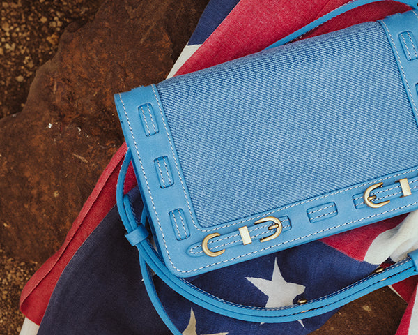 Close up of Denim blue handbag with brass hardware laying on an American Flag