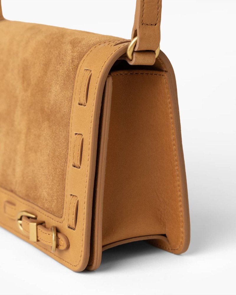 Close up of cognac suede handbag with brass hardware on a white background
