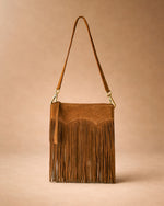 Brown suede handbag with fringe details on a beige background