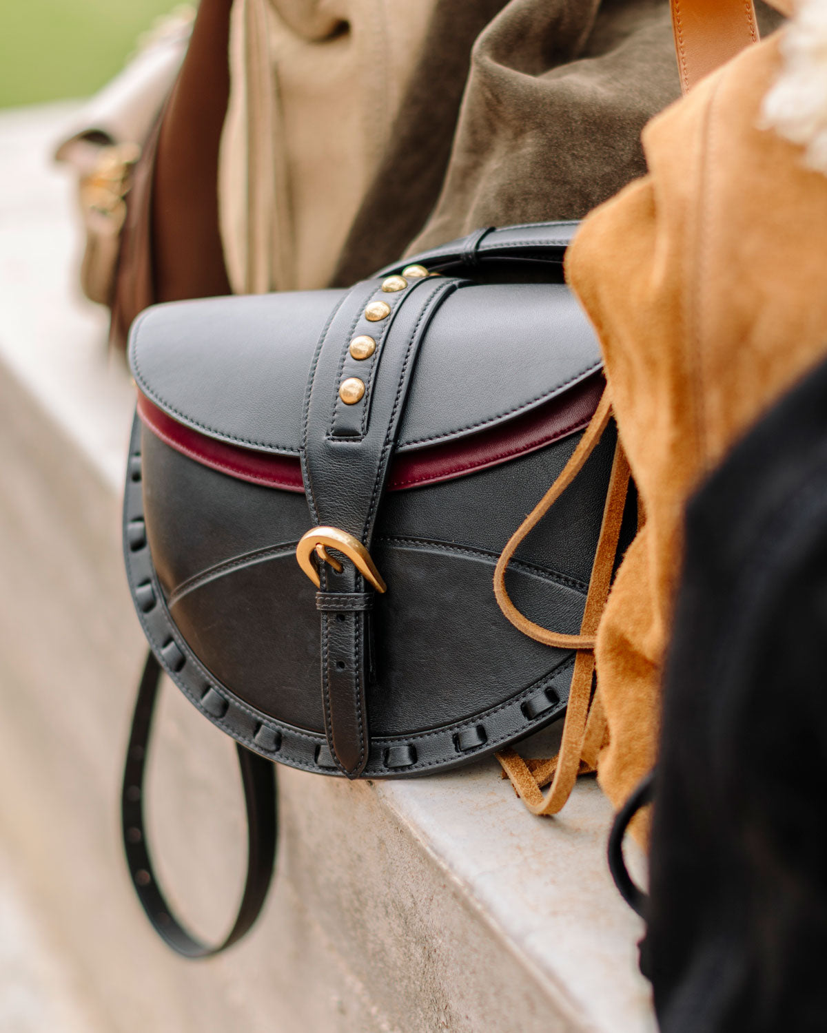 Black leather bag with gold studs and red interior lining on a stone surface.