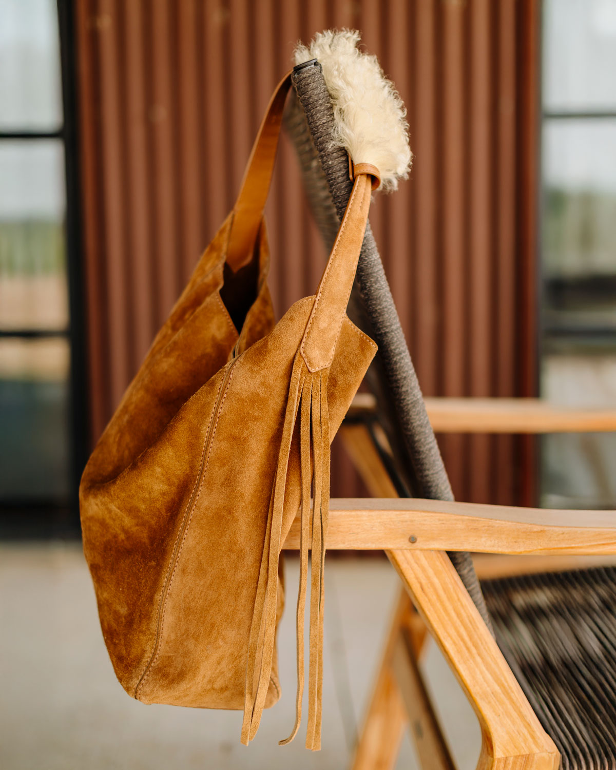 Brown suede bag with fringes hanging on a chair outdoors.