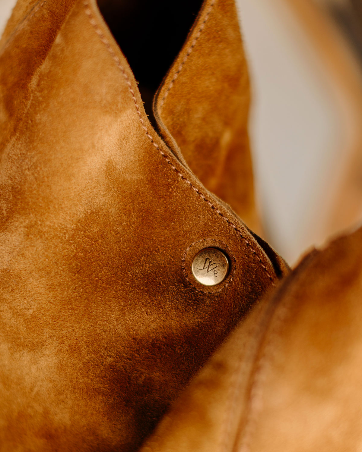 Close-up of a brown leather jacket with a button, featuring a brand logo.