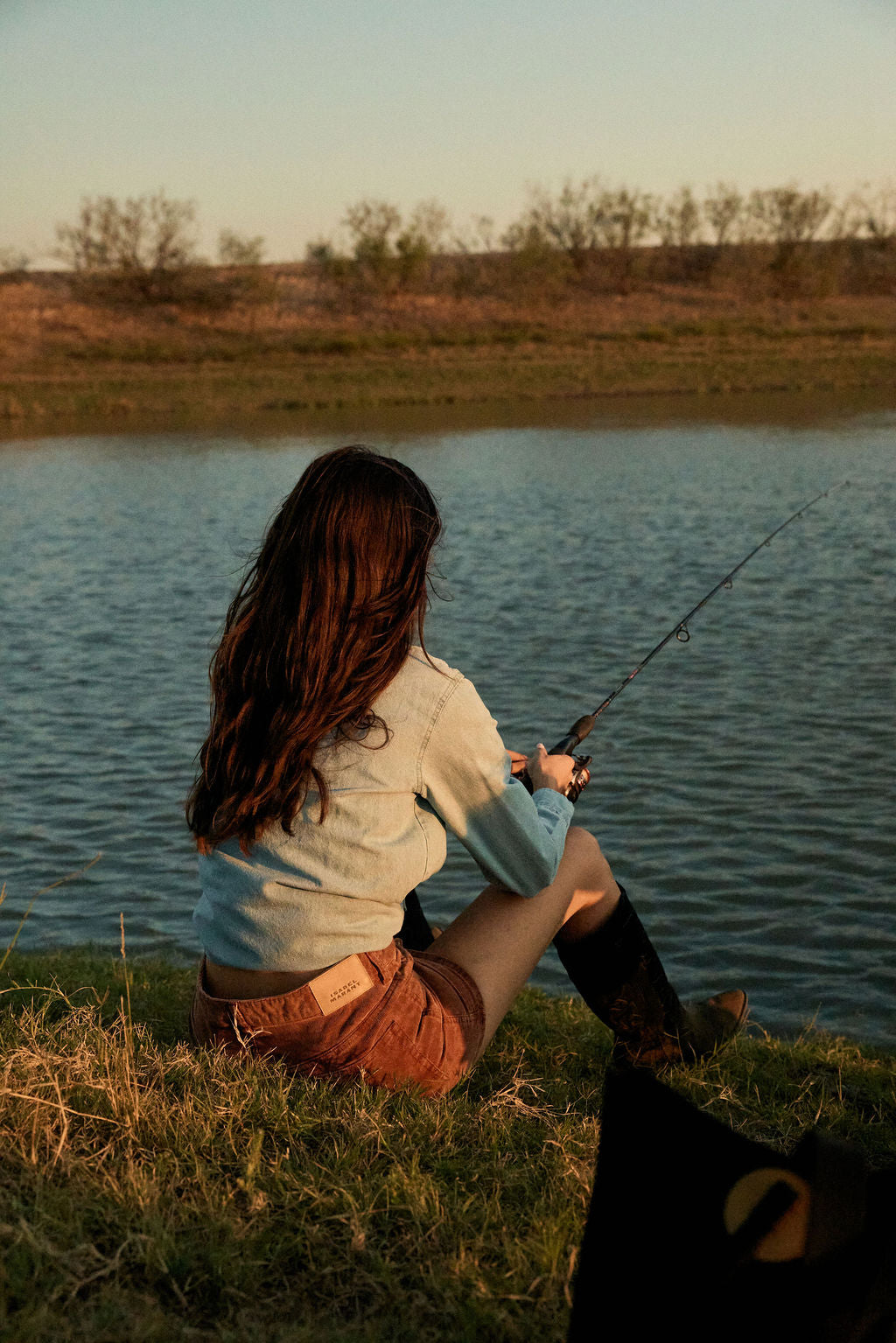 Woman fishing by a lake at sunset