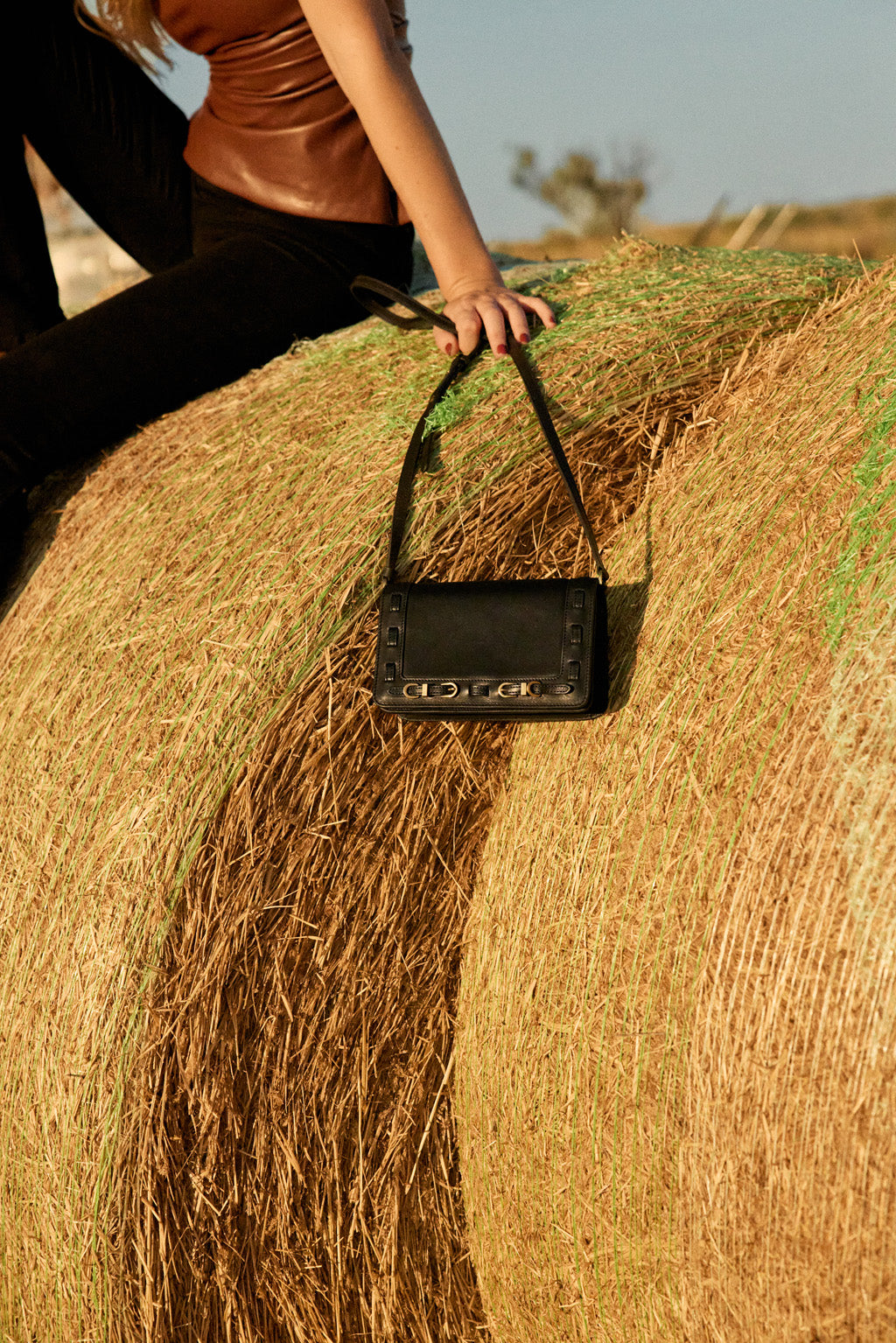 Woman holding a black handbag on a hay bale with a blurred background
