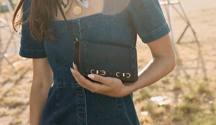 Person holding a black handbag with a blurred natural background