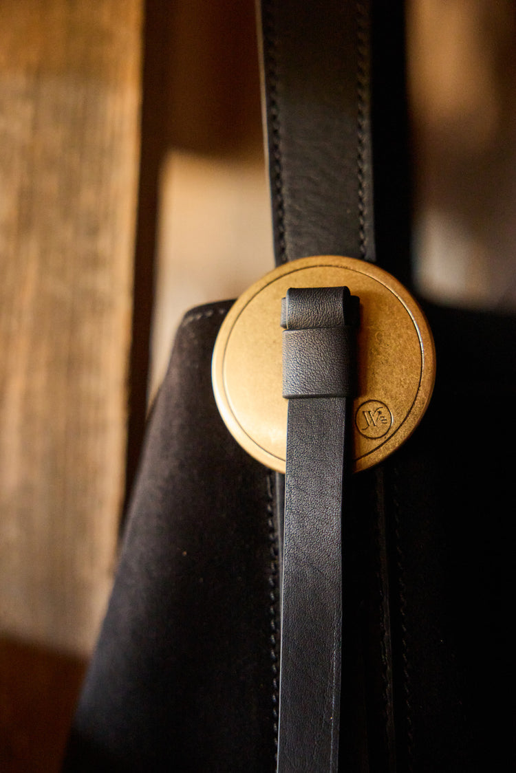 Close-up of a black leather strap with a brass concho on a blurred background