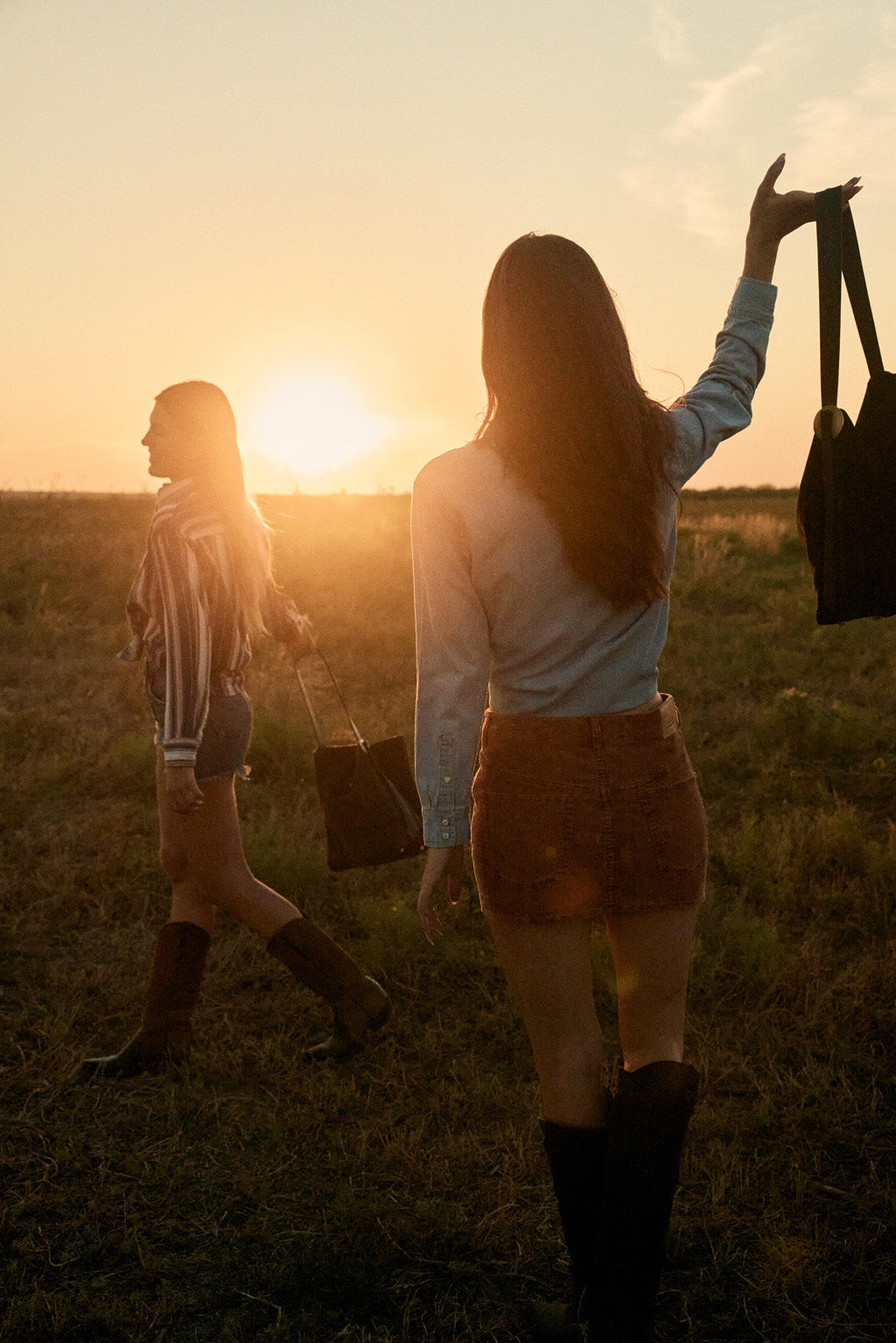 Two women walking in a field with the sun setting in the background