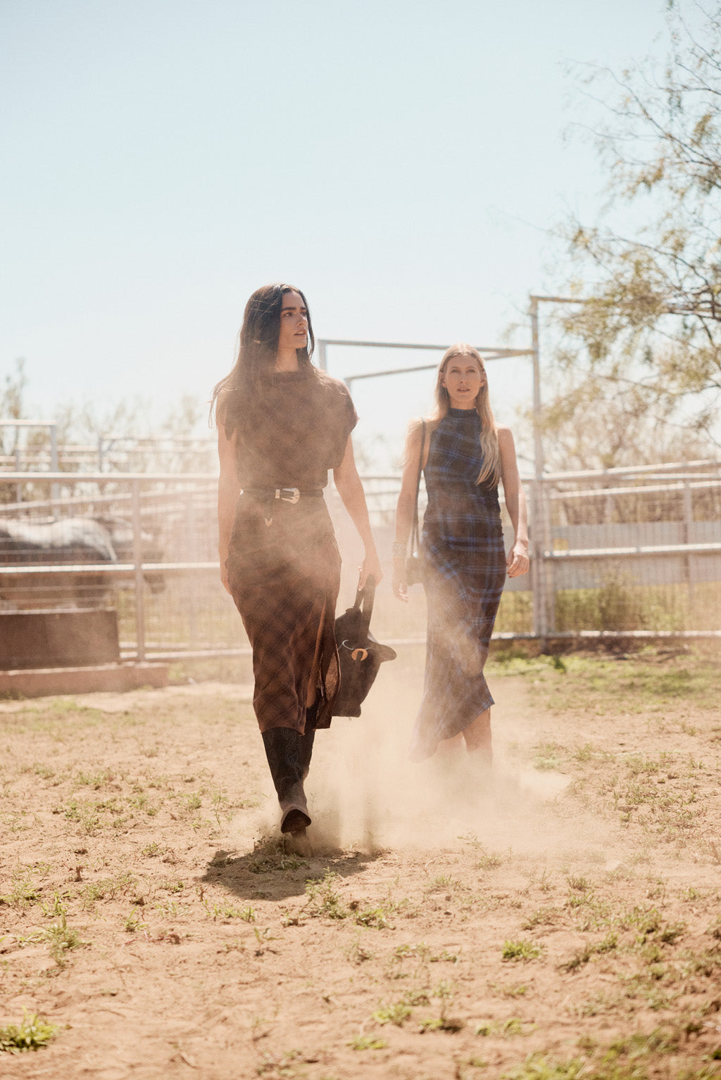 Two women walking on a dirt path with a fence and trees in the background