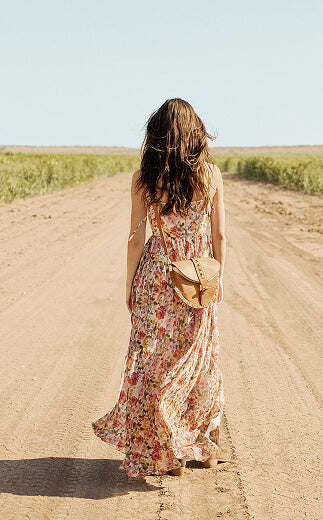 Woman in a floral dress walking away on a dirt road with a clear blue sky.