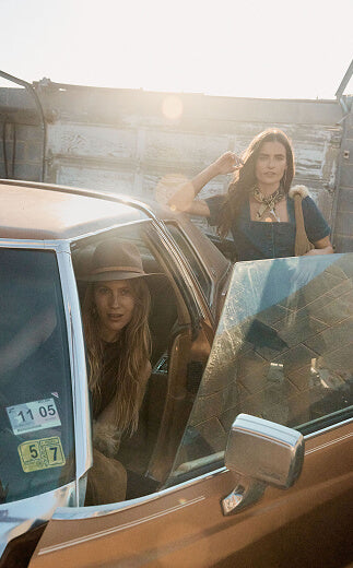Two women in a vintage car with a rustic background