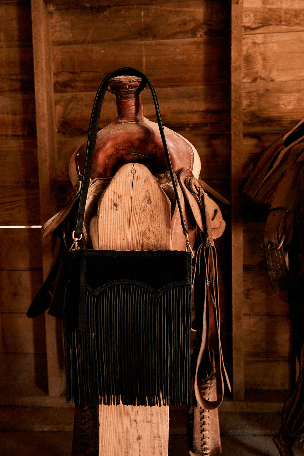 Black fringe bag with a horse saddle on a wooden background