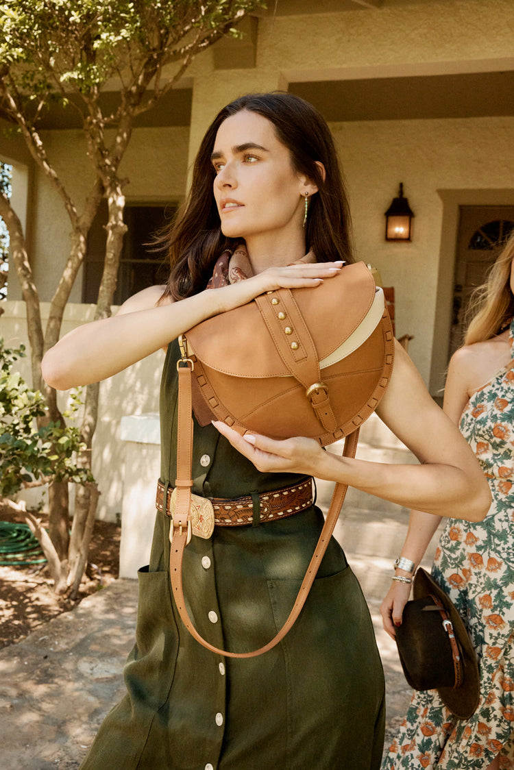 Woman wearing a green outfit with a brown leather handbag outdoors.