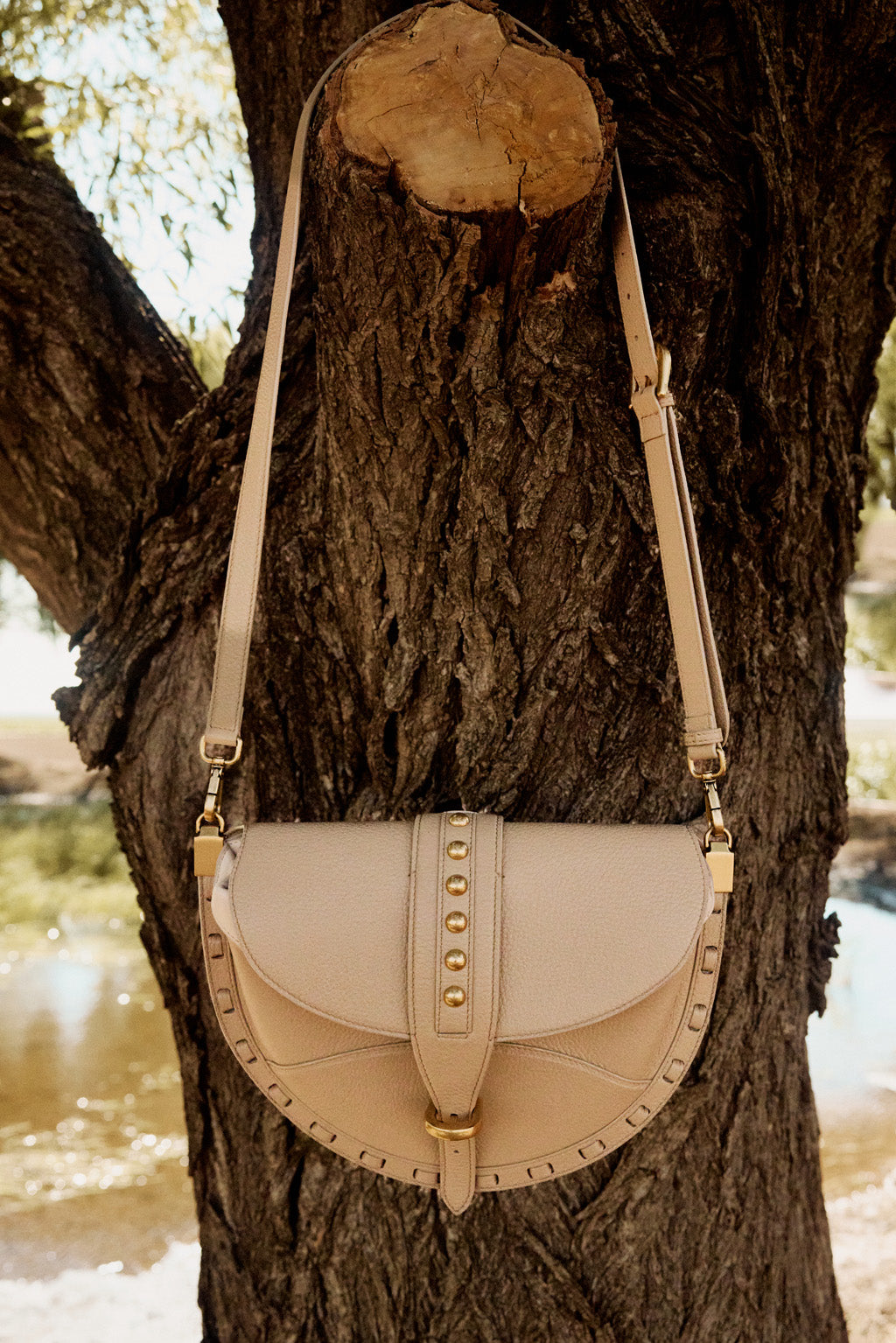 Beige handbag with gold accents hanging on a tree