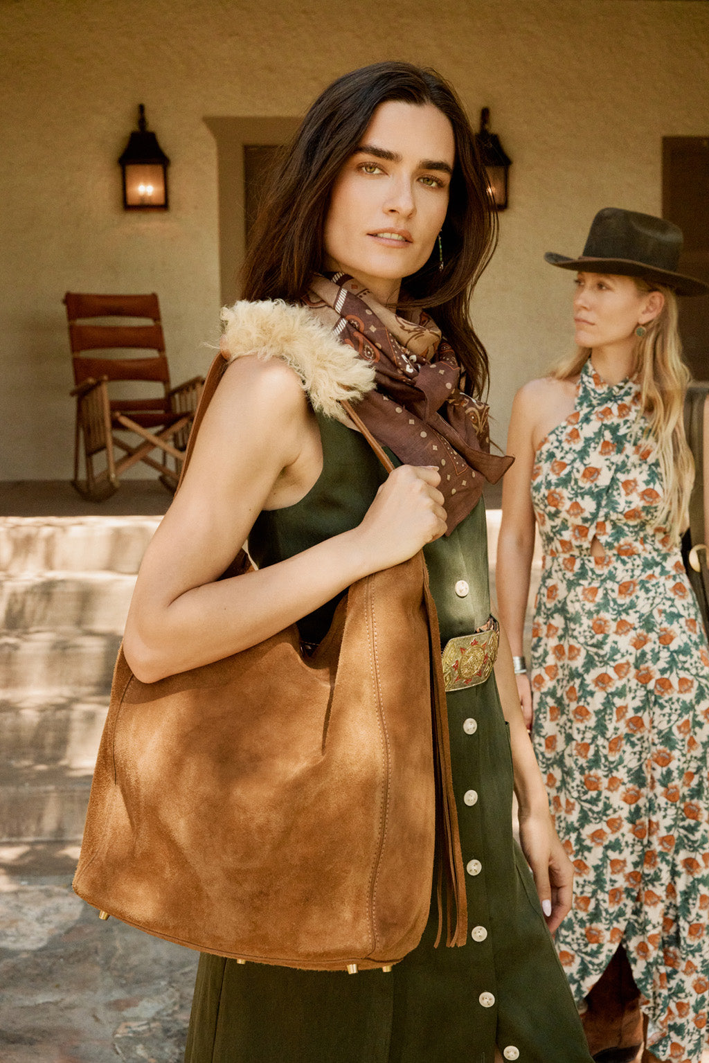 Two women standing outdoors with one holding a brown leather bag.
