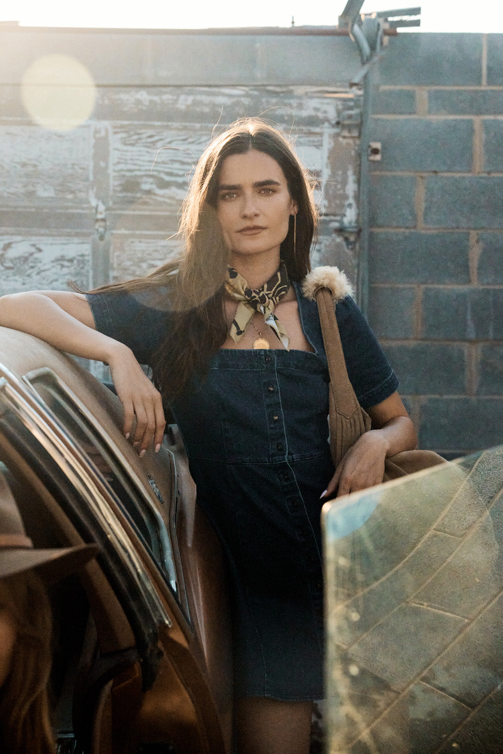 Woman wearing a handbag standing by a car with a textured wall in the background